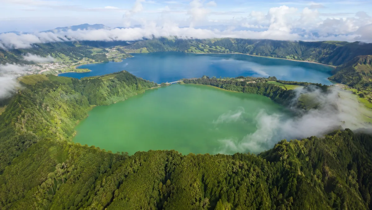 Vista aérea de las lagunas gemelas de Sete Cidades, una verde y otra azul, dentro del cráter volcánico entre laderas verdes y jirones de niebla, São Miguel, Azores