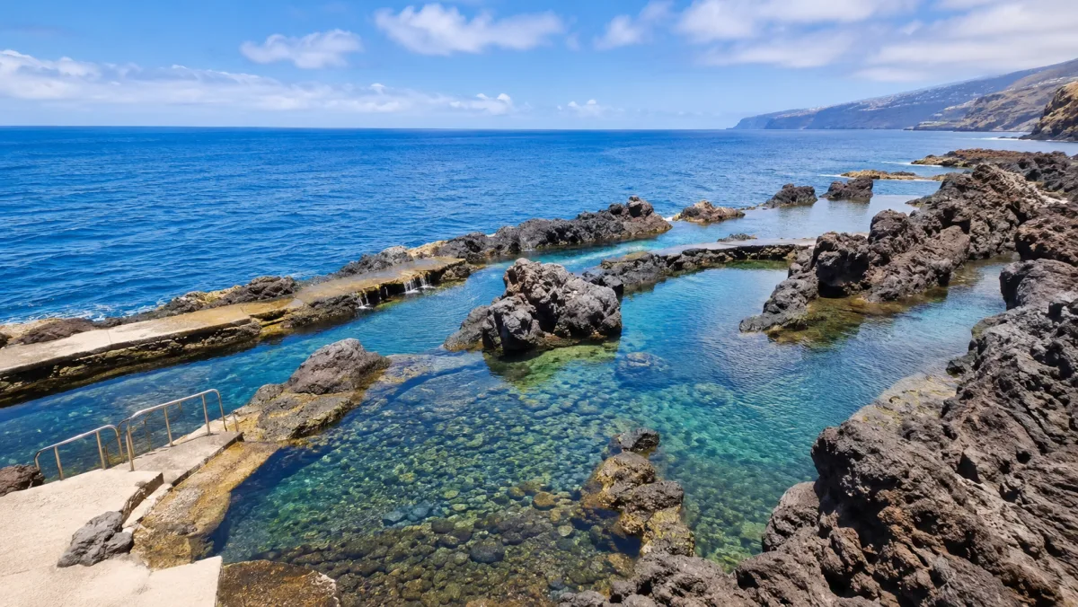 Piscinas naturales de roca volcánica en la costa sur de Madeira con agua transparente entre lava negra, escaleras de acceso y el Atlántico azul al fondo