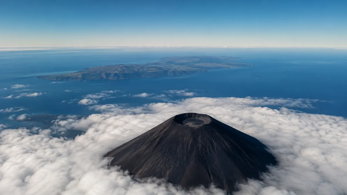 Vista aérea del cono volcánico negro del Pico emergiendo sobre un mar de nubes, con las islas de Faial y São Jorge al fondo, Azores