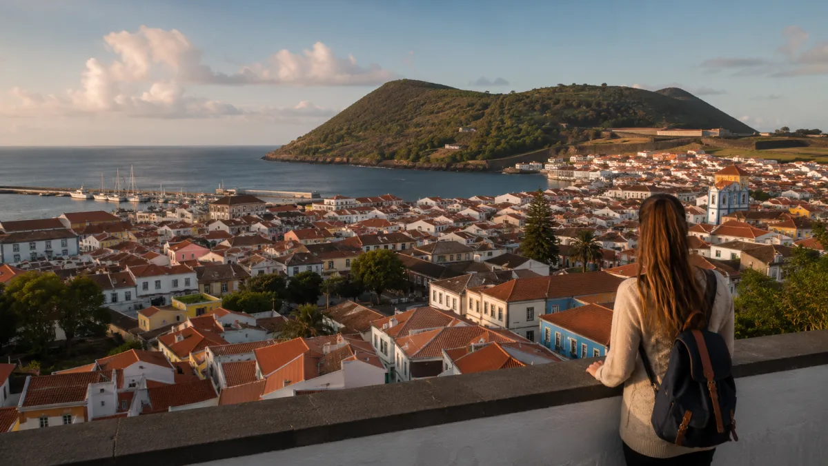 Una viajera de espaldas contempla desde un mirador Angra do Heroísmo con sus casas de colores, la bahía y el Monte Brasil al atardecer, Terceira, Azores
