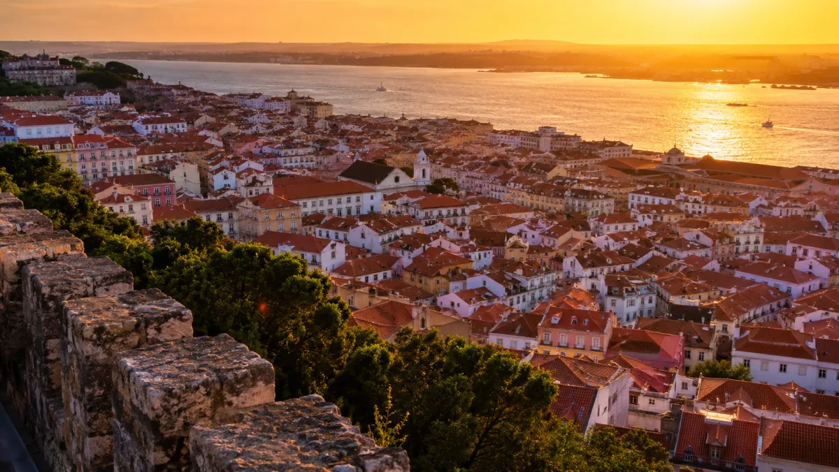 Los tejados naranjas de Alfama descendiendo hacia el Tajo dorado al atardecer, vistos desde las murallas del Castelo de São Jorge