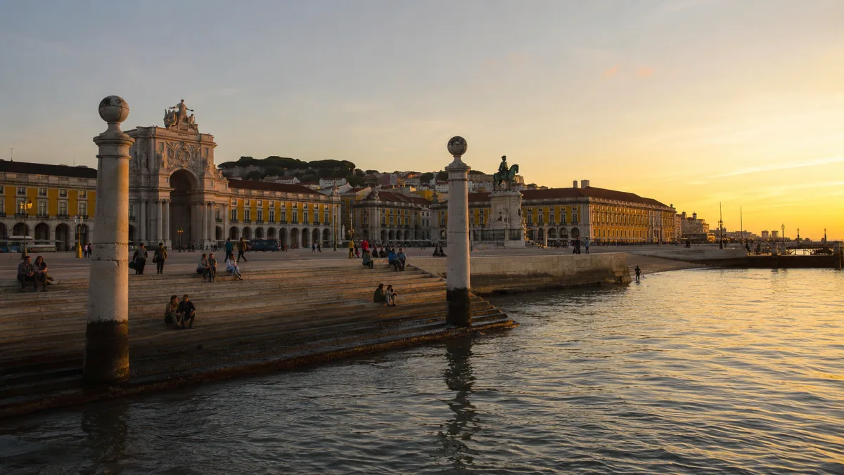 El arco triunfal y las fachadas amarillas de la Praça do Comércio al atardecer, vistos desde el Cais das Colunas a orillas del Tajo