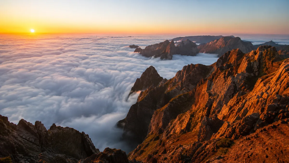 Amanecer sobre un mar de nubes desde el Pico do Areeiro: crestas de basalto iluminadas de naranja emergiendo por encima de las nubes
