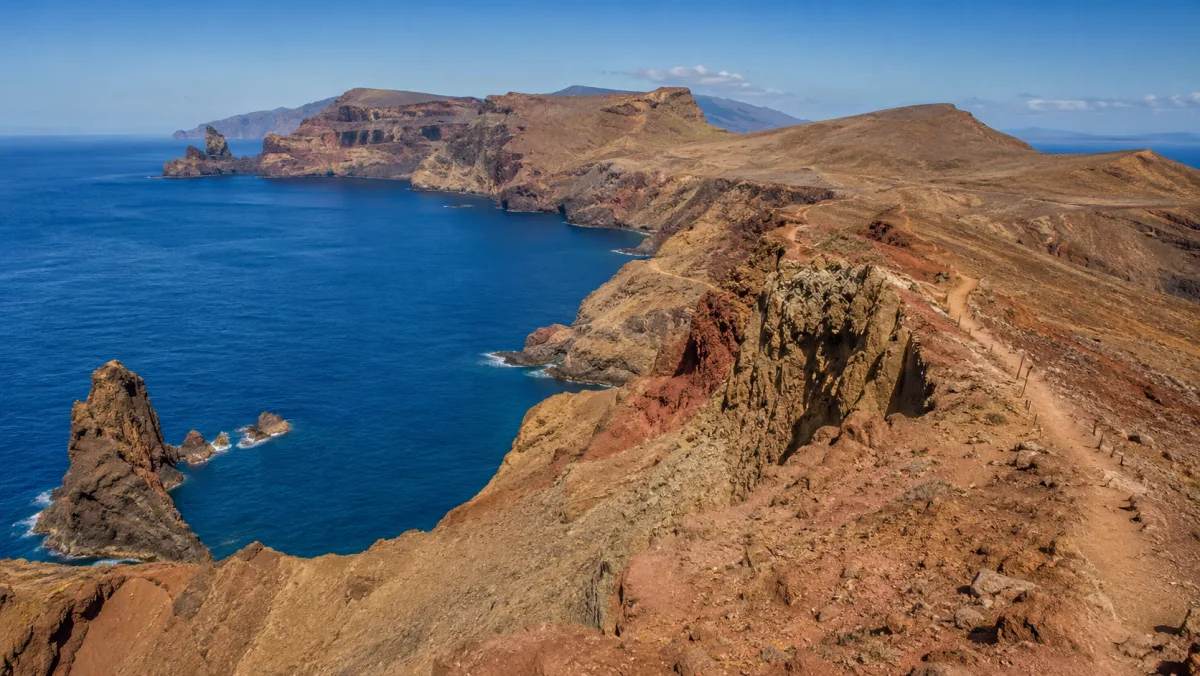 Los acantilados rojizos y ocres de la península de la Ponta de São Lourenço cayendo al Atlántico azul, con un sendero recorriendo la cresta