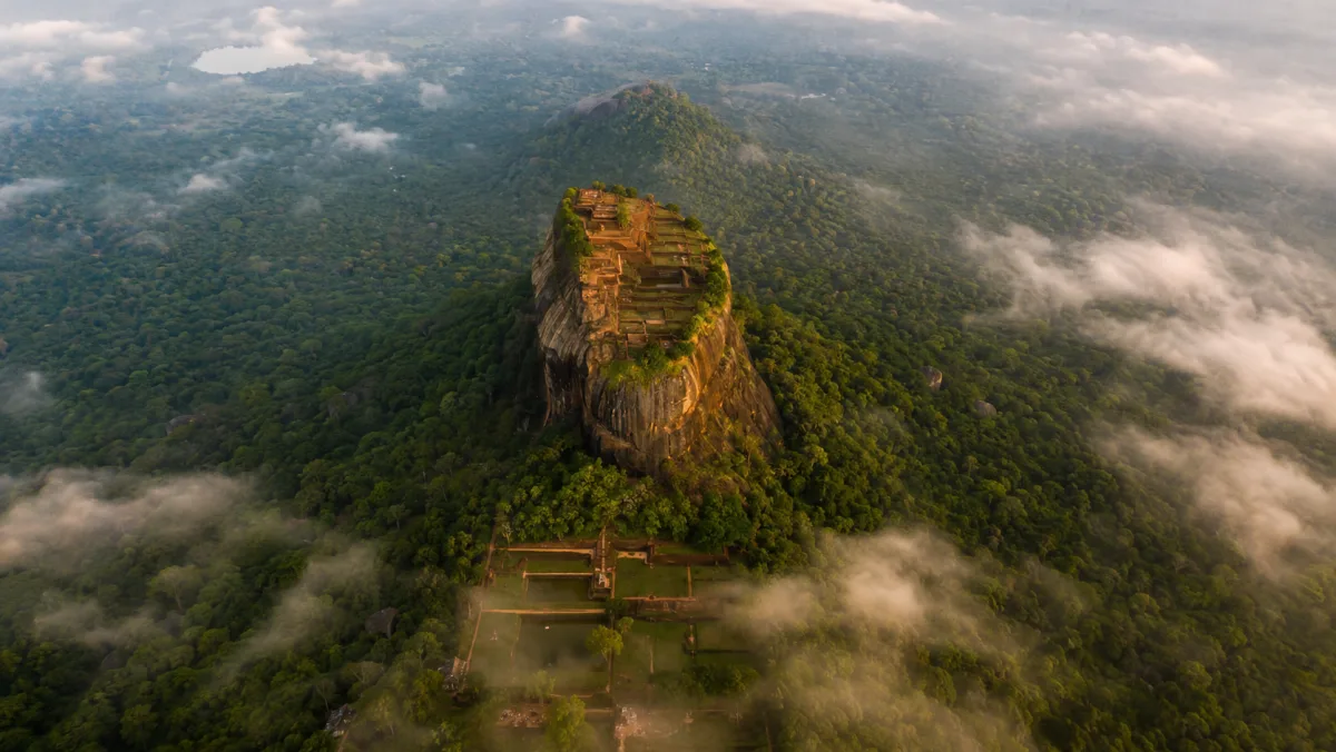 Vista aérea de la roca-fortaleza de Sigiriya (Lion Rock) de cima plana emergiendo entre la selva verde y las nubes al amanecer, Sri Lanka